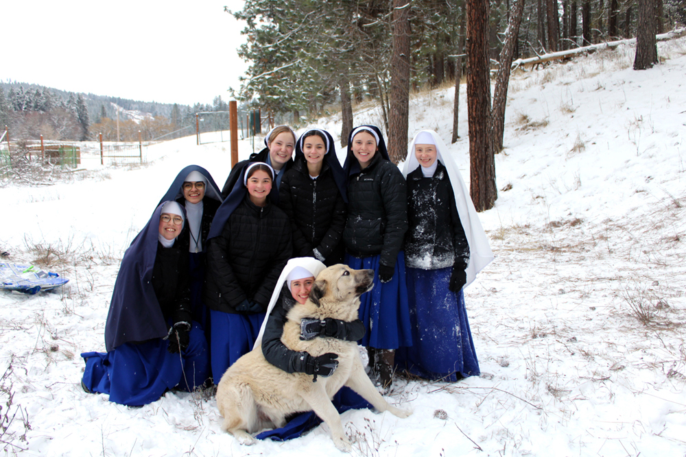 The postulants and novices gather for a group photo after an afternoon of sledding. The dog, it appears, would rather be guarding the cows and sheep.