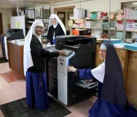 Sr. Mary Agatha shows Sr. Maria Bosco and Sr. Noel Marie on how to print envelopes.